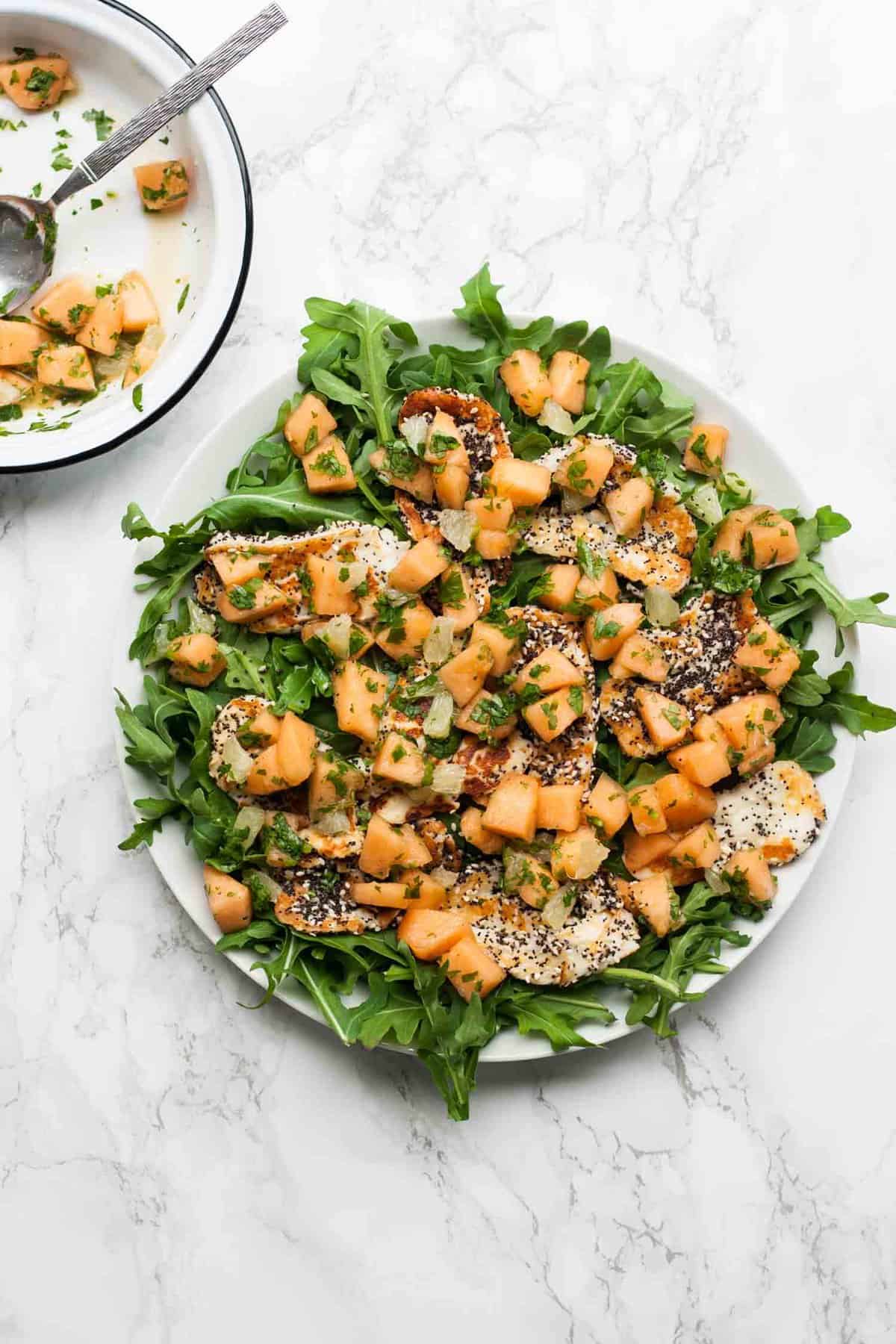 A platter with melon scattered on top of a halloumi salad.