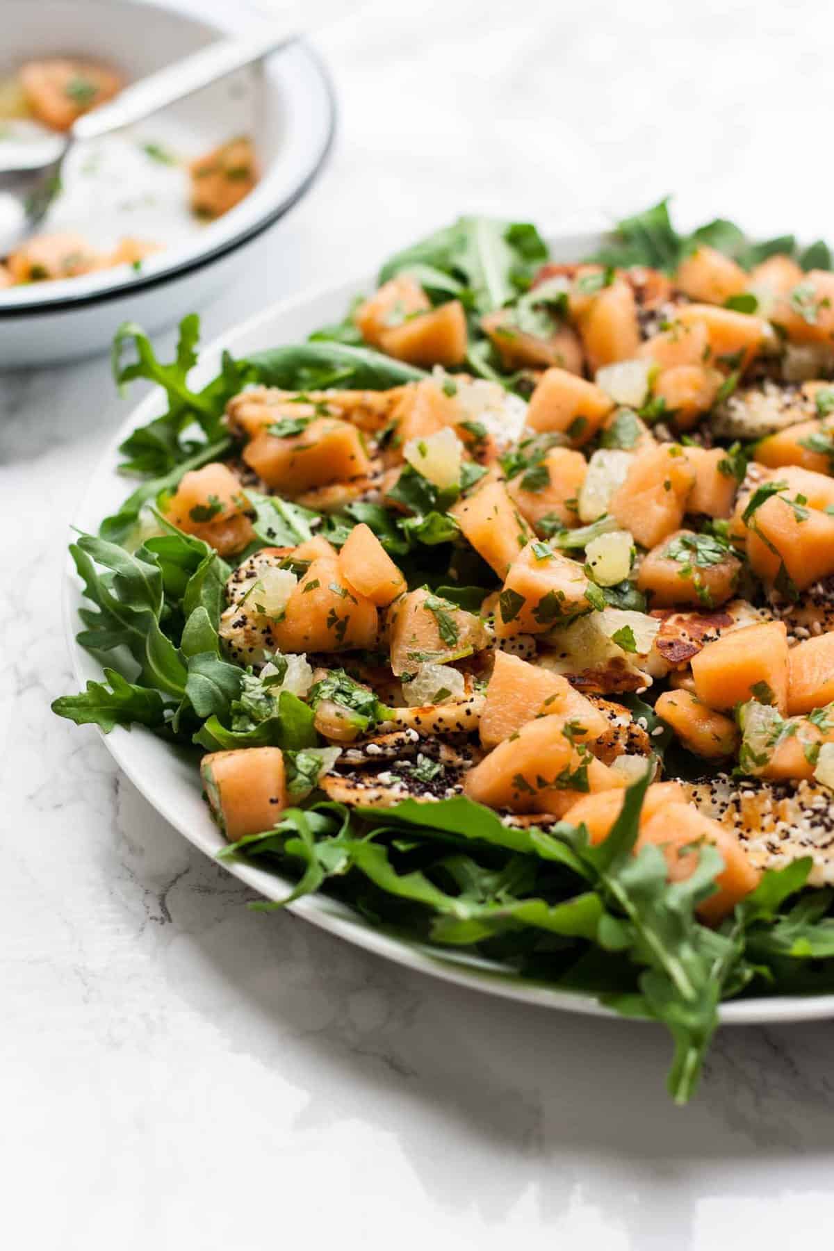 Close up of halloumi and melon on a platter with salad greens.