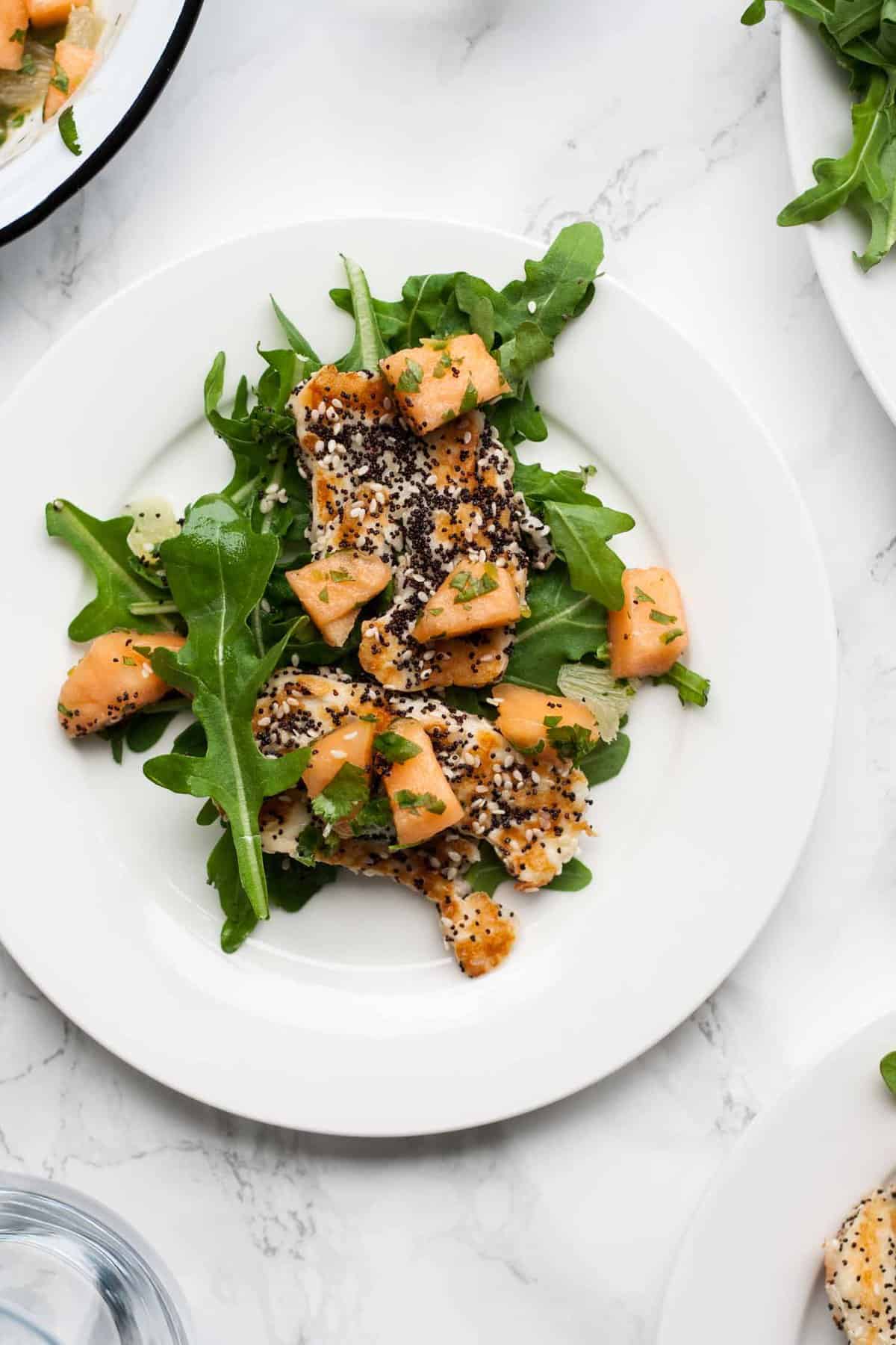 A close up of melon halloumi lime salad on a white plate.