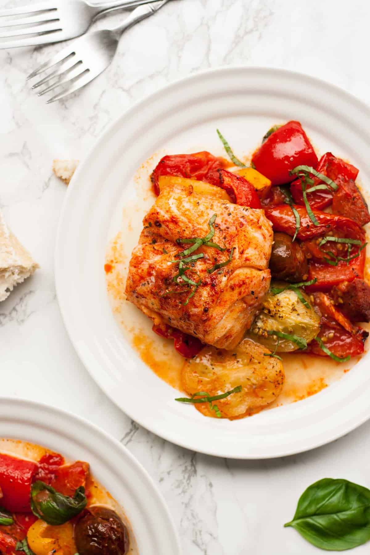 A plate with a cod fillet served atop roasted tomatoes. 