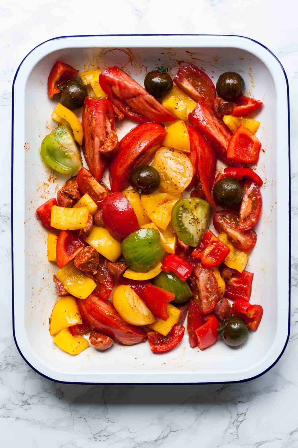 A baking sheet with fresh tomatoes chopped and dressed and seasoned before baking.