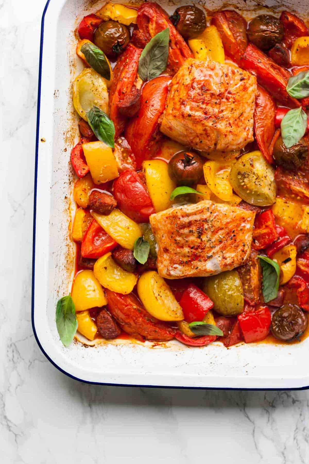 Cod fillets roasted on top of the baked tomatoes in a baking sheet.