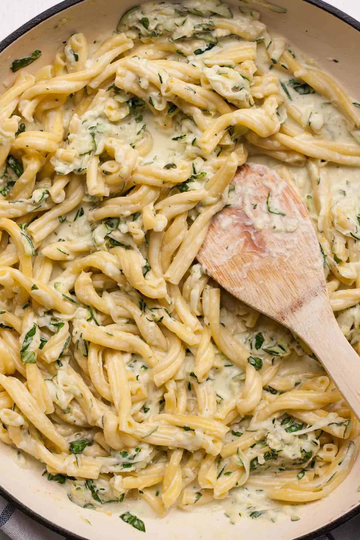 Close up of creamy pasta with a wooden spatula.