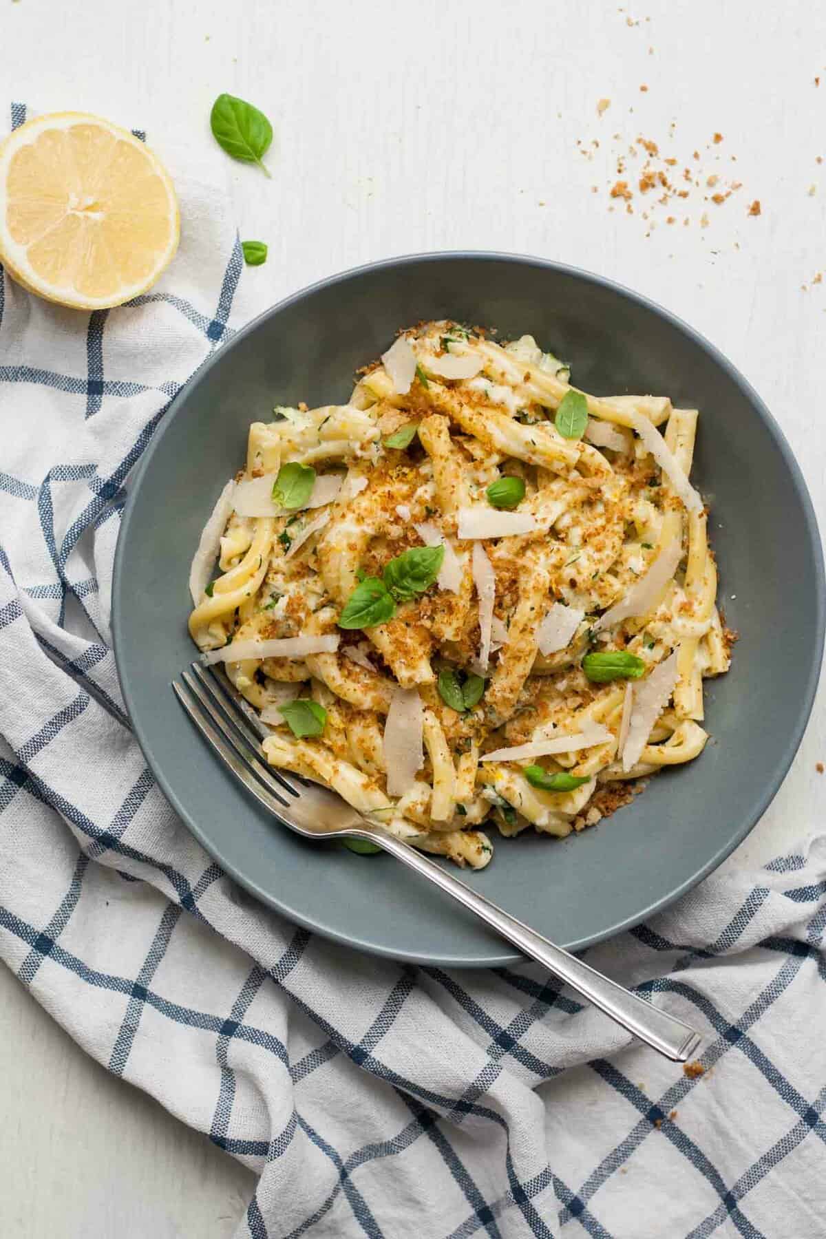 A bowl of zucchini pasta with a fork on top of a checked napkin.