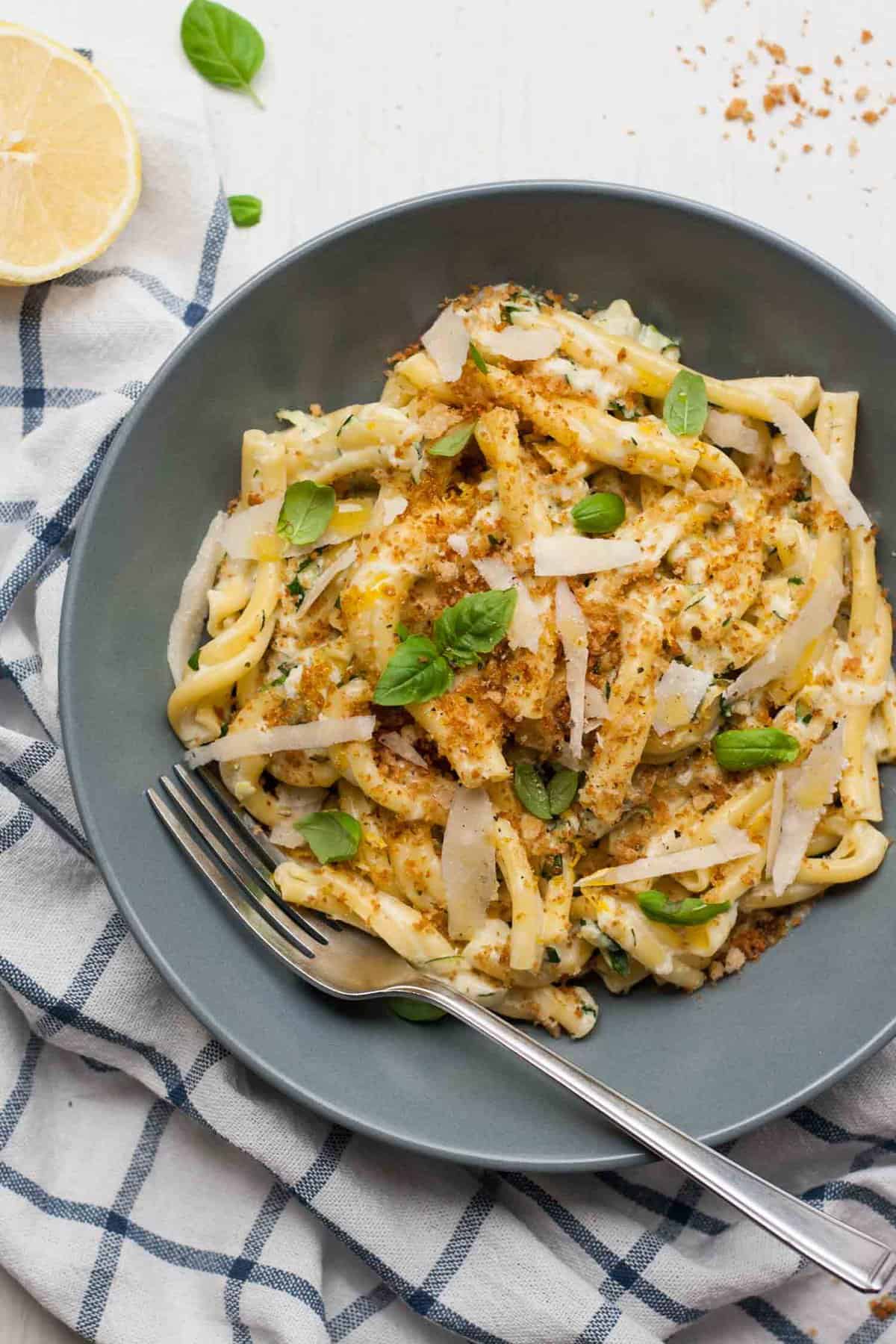 A bowl with pasta in served with parmesan shavings and a fork.