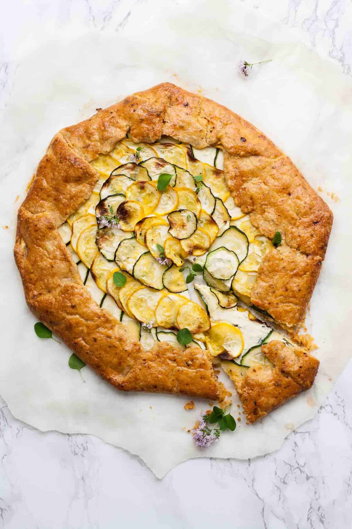 Overhead of courgette galette on parchment with a slice cut from it.