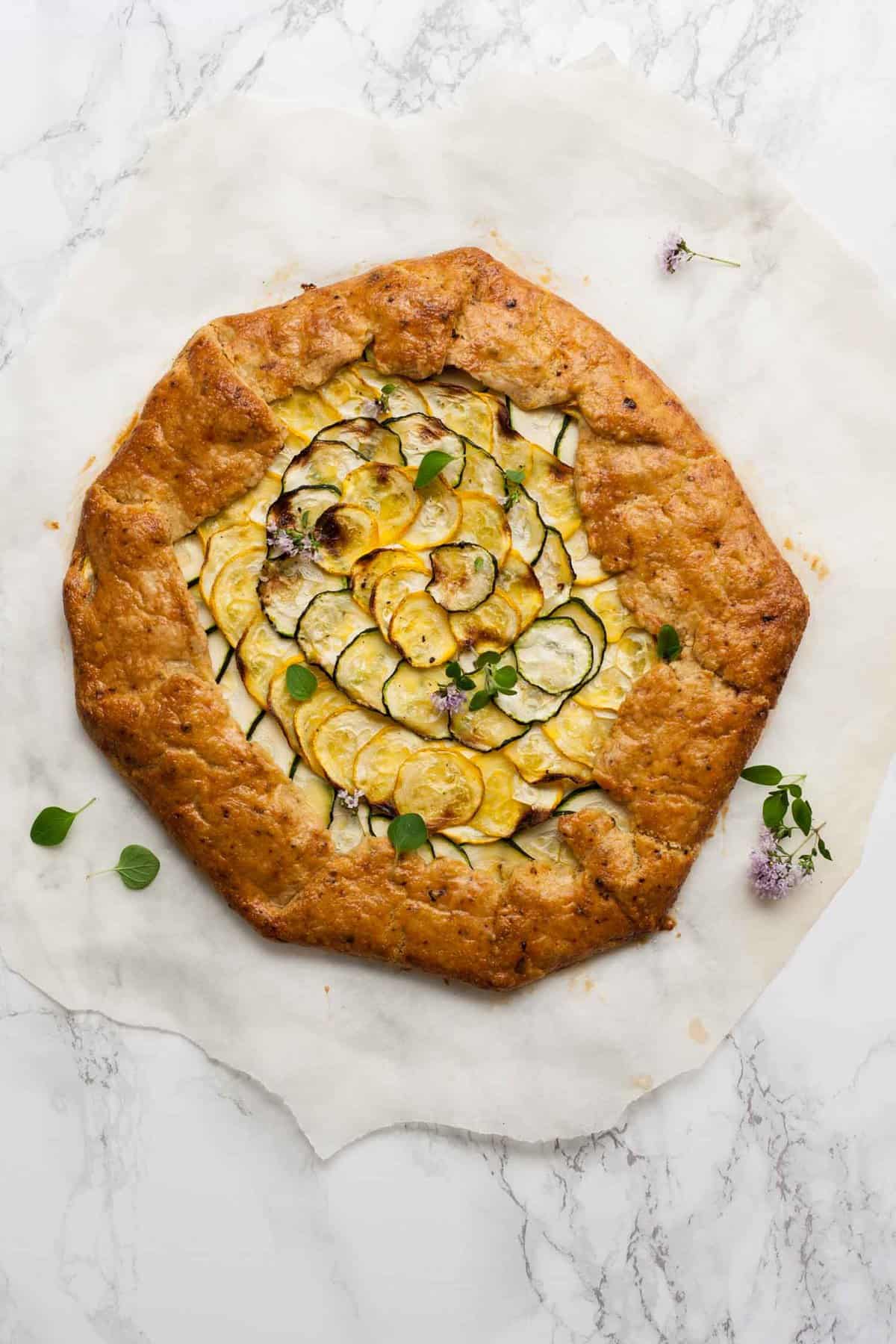 A courgette galette on parchment paper on top of a marble work surface.