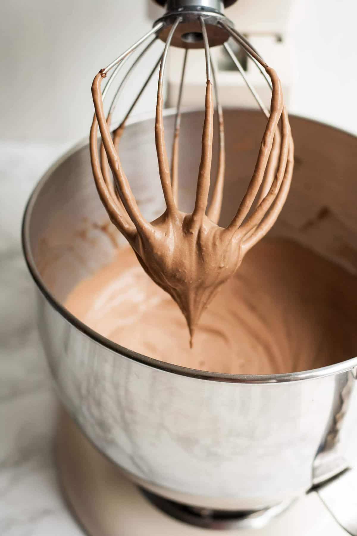 A whisk with whipped mocha cream on the end with a metal below underneath.