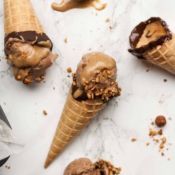 Three waffle cones on a marble work top with mocha ice cream and nuts around.