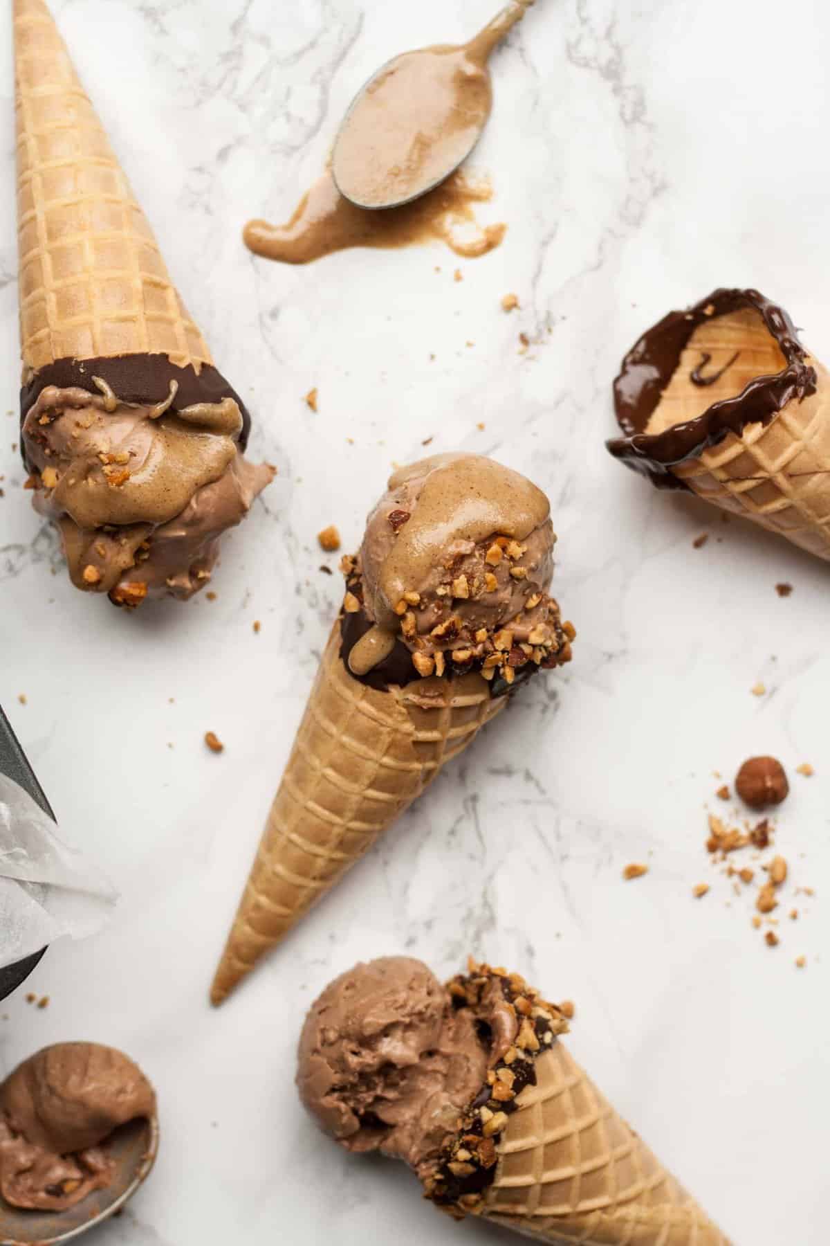 Three waffle cones on a marble work top with mocha ice cream and nuts around.