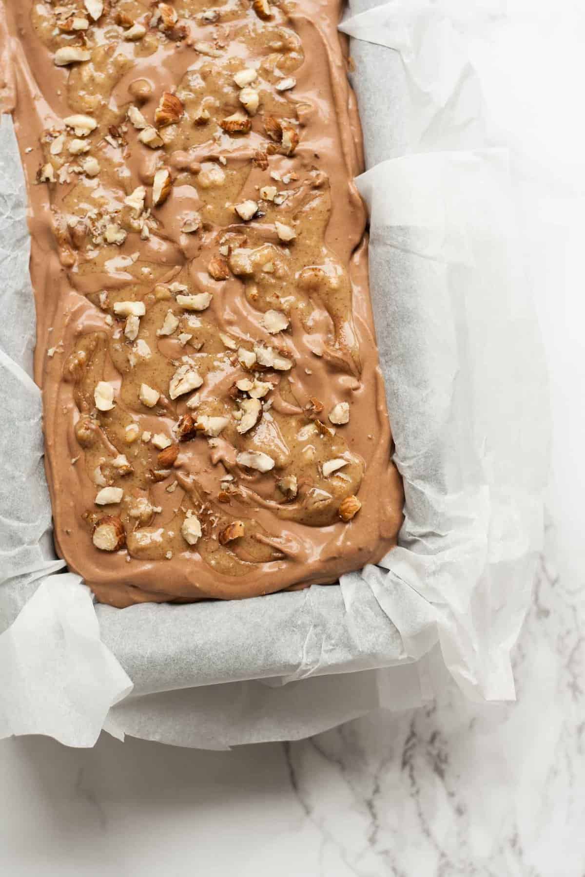 Mocha ice cream mix in a loaf tin lined with parchment paper with nuts on top.