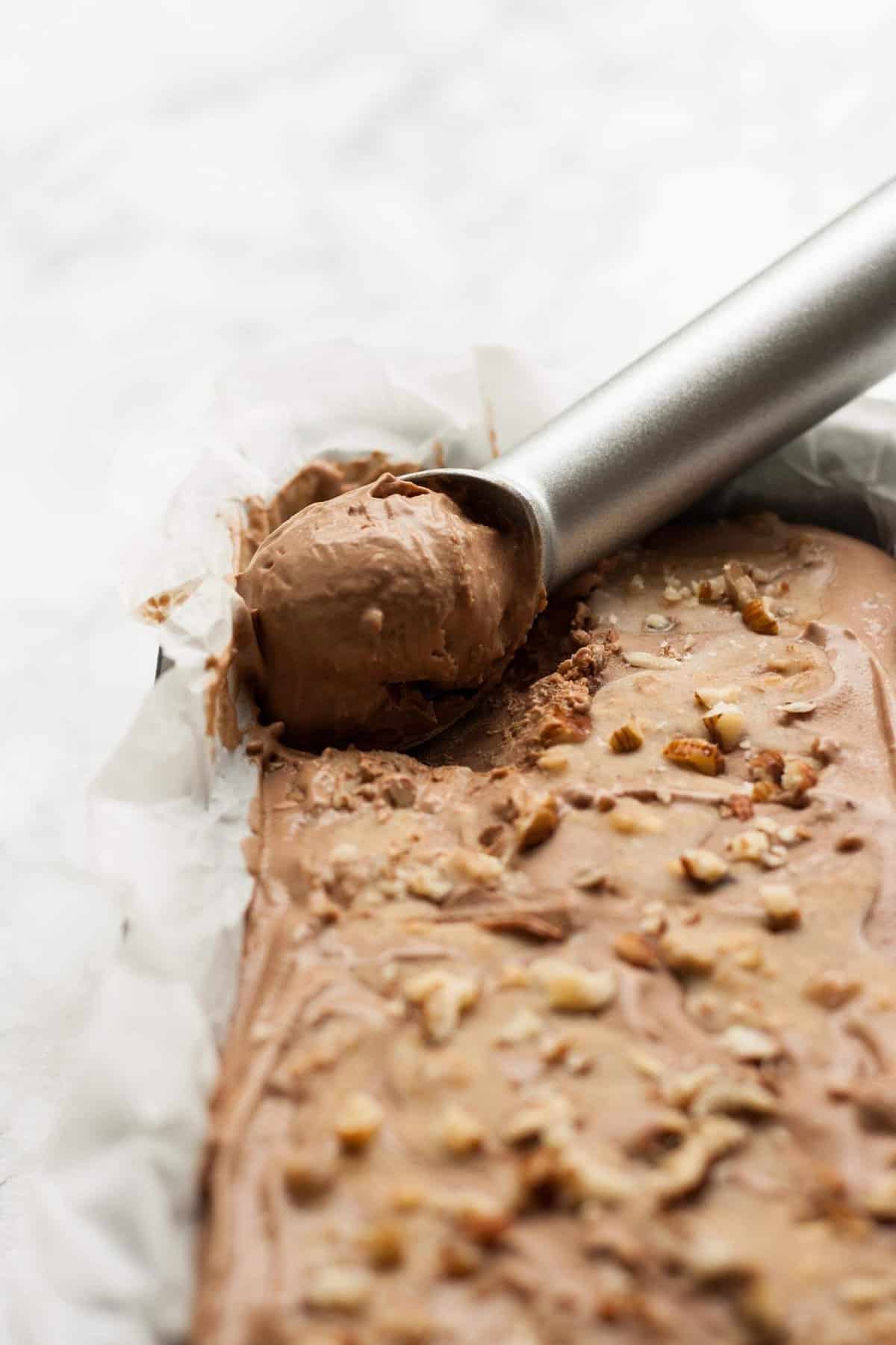 An ice cream scoop scooping mocha ice cream from the loaf tin lined with parchment.
