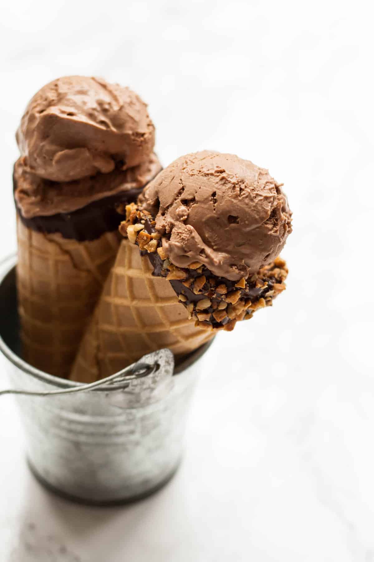 Two waffle cones with mocha ice cream on top in a little tin bucket.