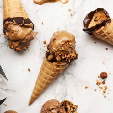 Mocha Ice cream served in waffle cones on a marble surface with chopped hazelnuts.