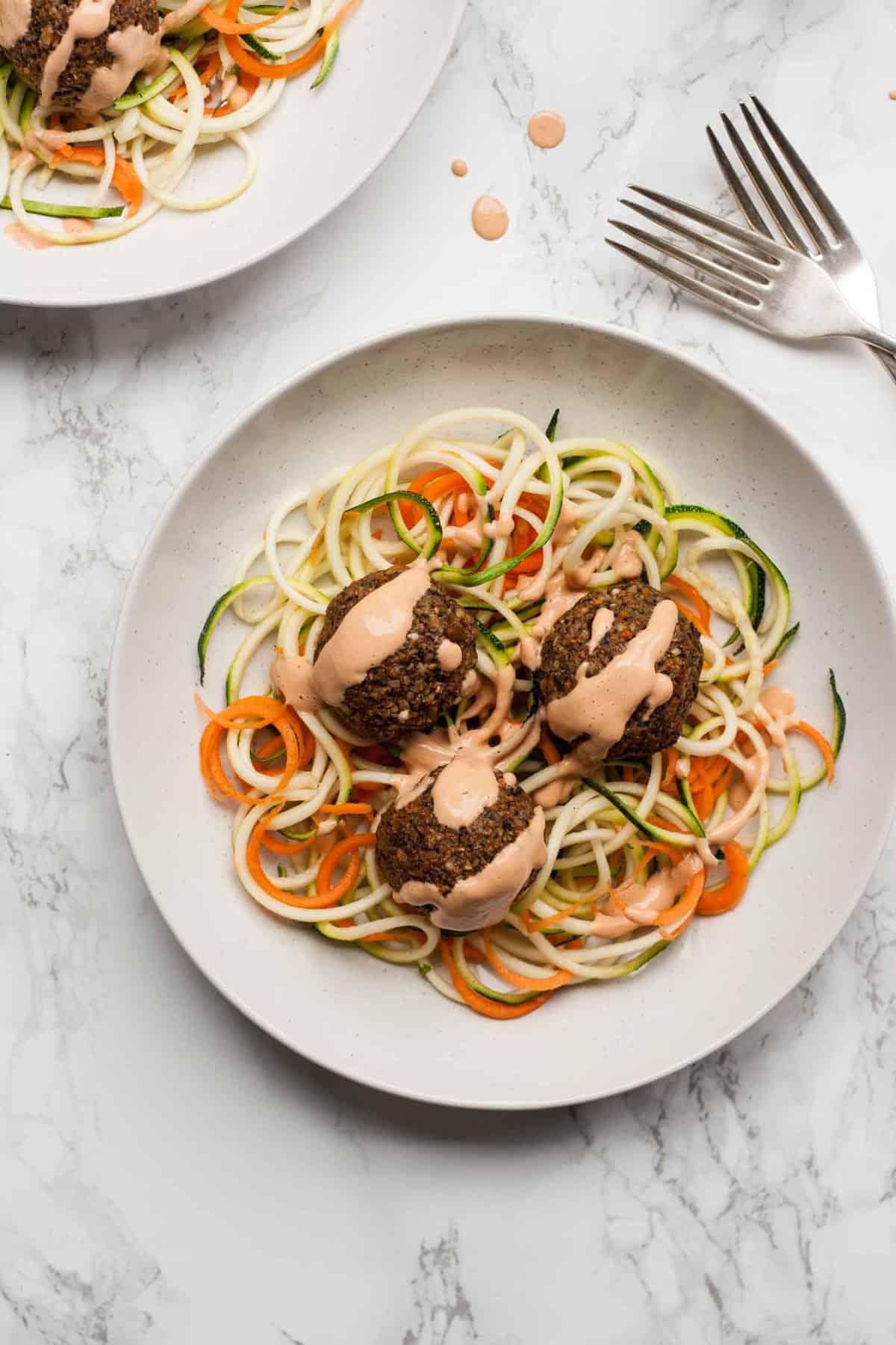 Vegan meatballs dressed with a sauce on zoodles with a fork.