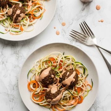 Two plates of vegan meatballs on zoodles with sauce on top and forks to the side.