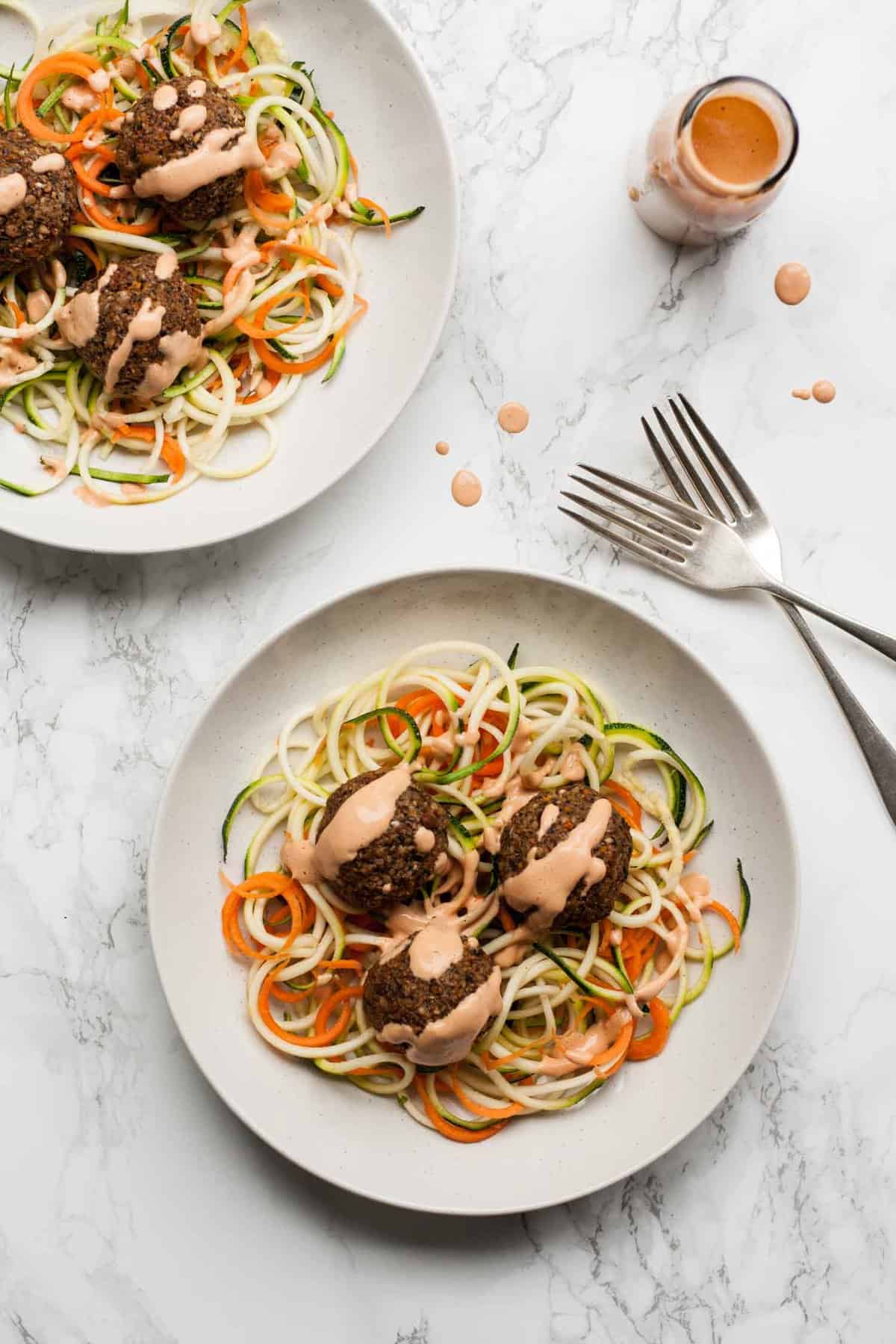 Two plates of vegan meatballs on zoodles with sauce on top and forks to the side.