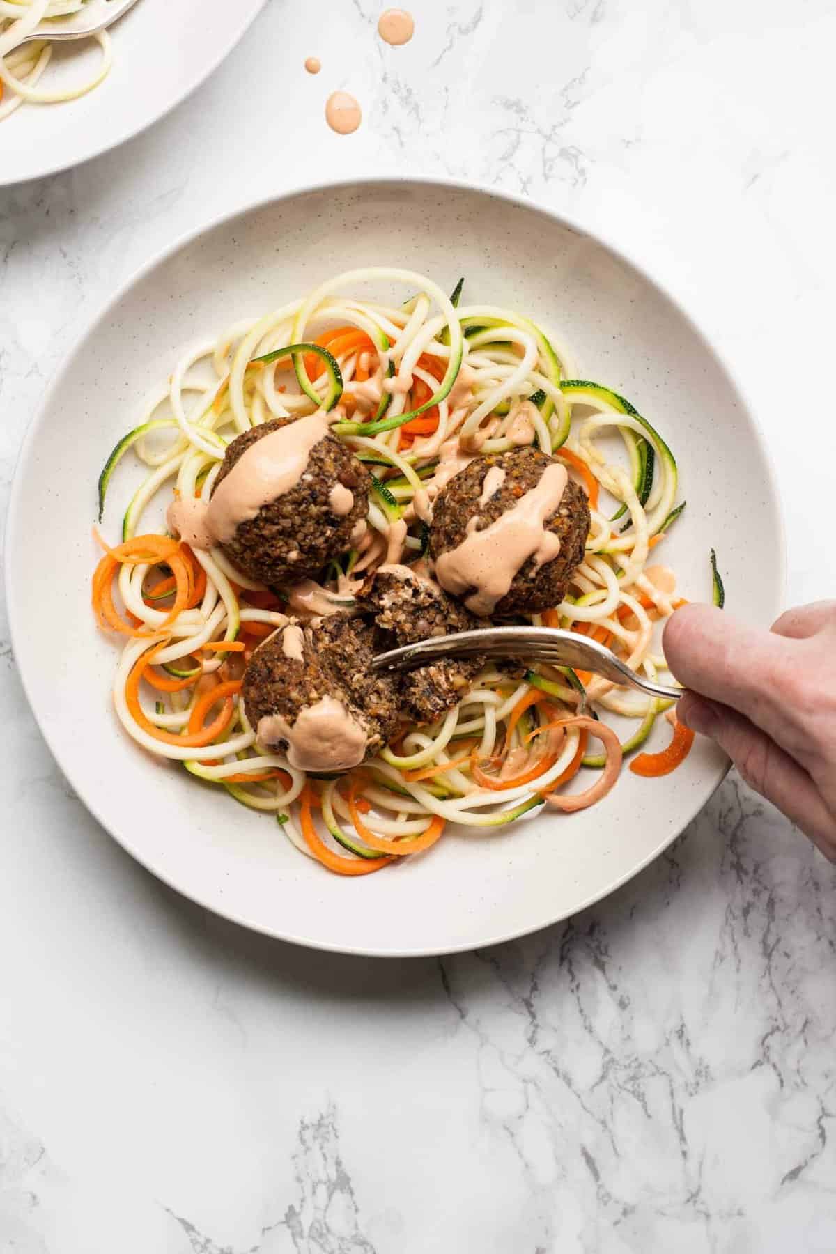 A person cutting a vegan meatball open with a fork served on a plate.