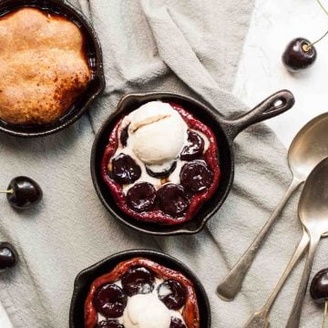 three mini cast iron skillets with cherry tarte tatin in and ice cream on top.