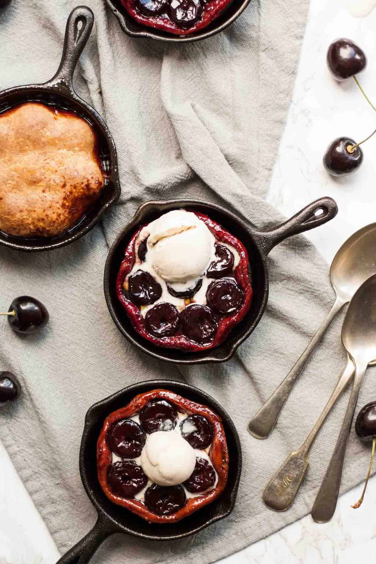 three mini cast iron skillets with cherry tarte tatin in and ice cream on top.