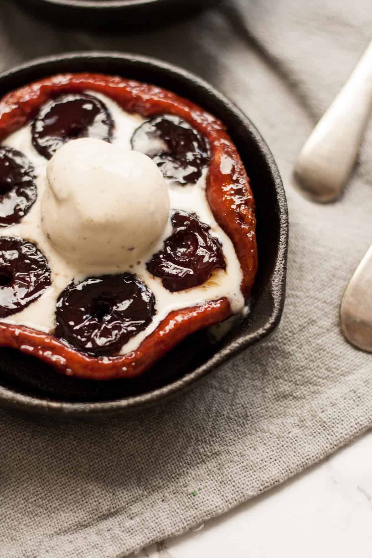 A mini cast iron skillet with cherry tarte tatin with ice cream on top.