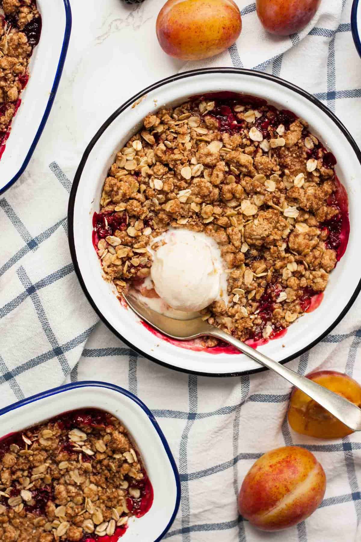 A dish with a fruit crips in with a spoon of ice cream on top and spoon inside.