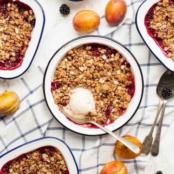 Multiple dishes of plum and blackberry crumble, one with ice cream on top with a spoon.