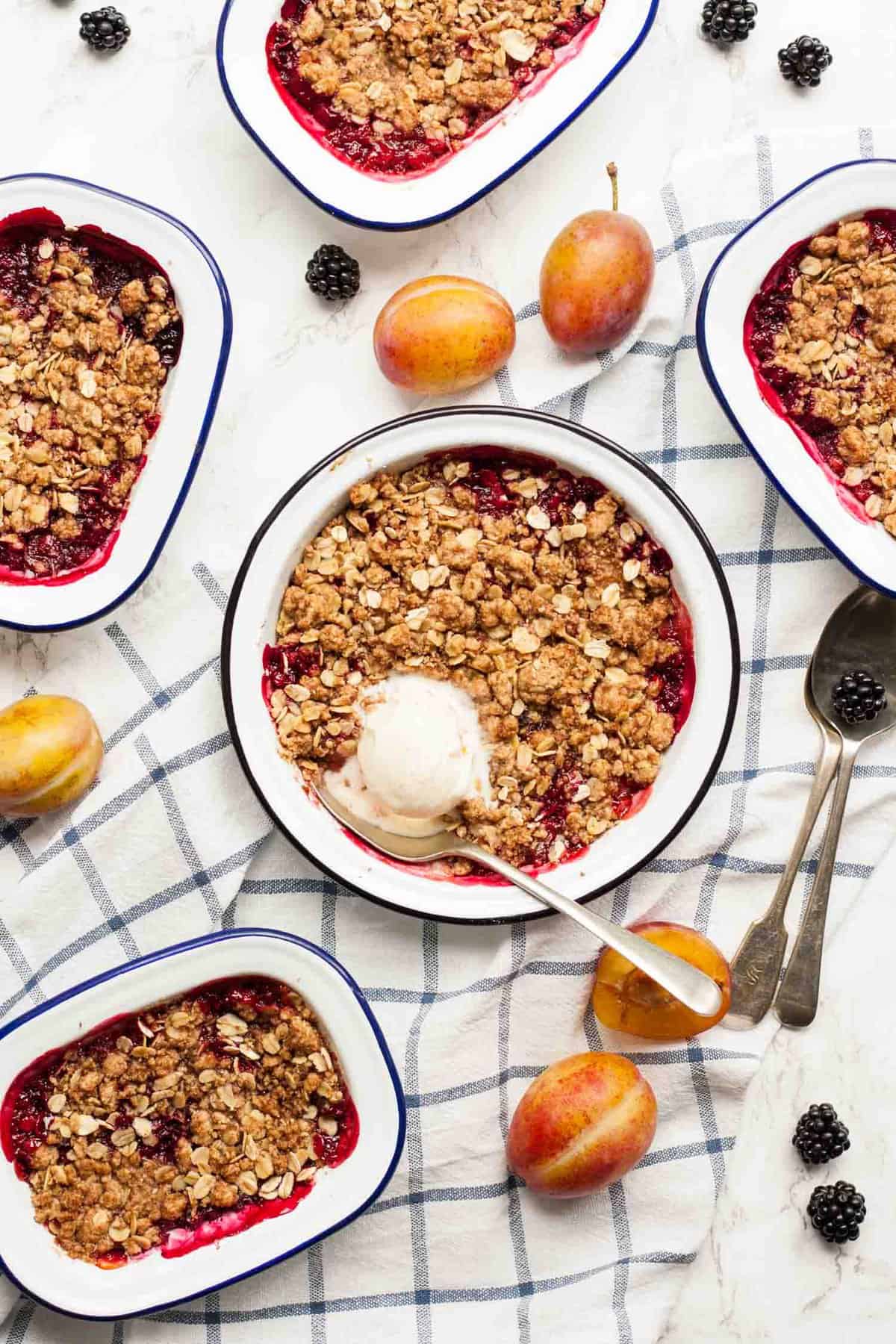 Multiple dishes of plum and blackberry crumble, one with ice cream on top with a spoon.