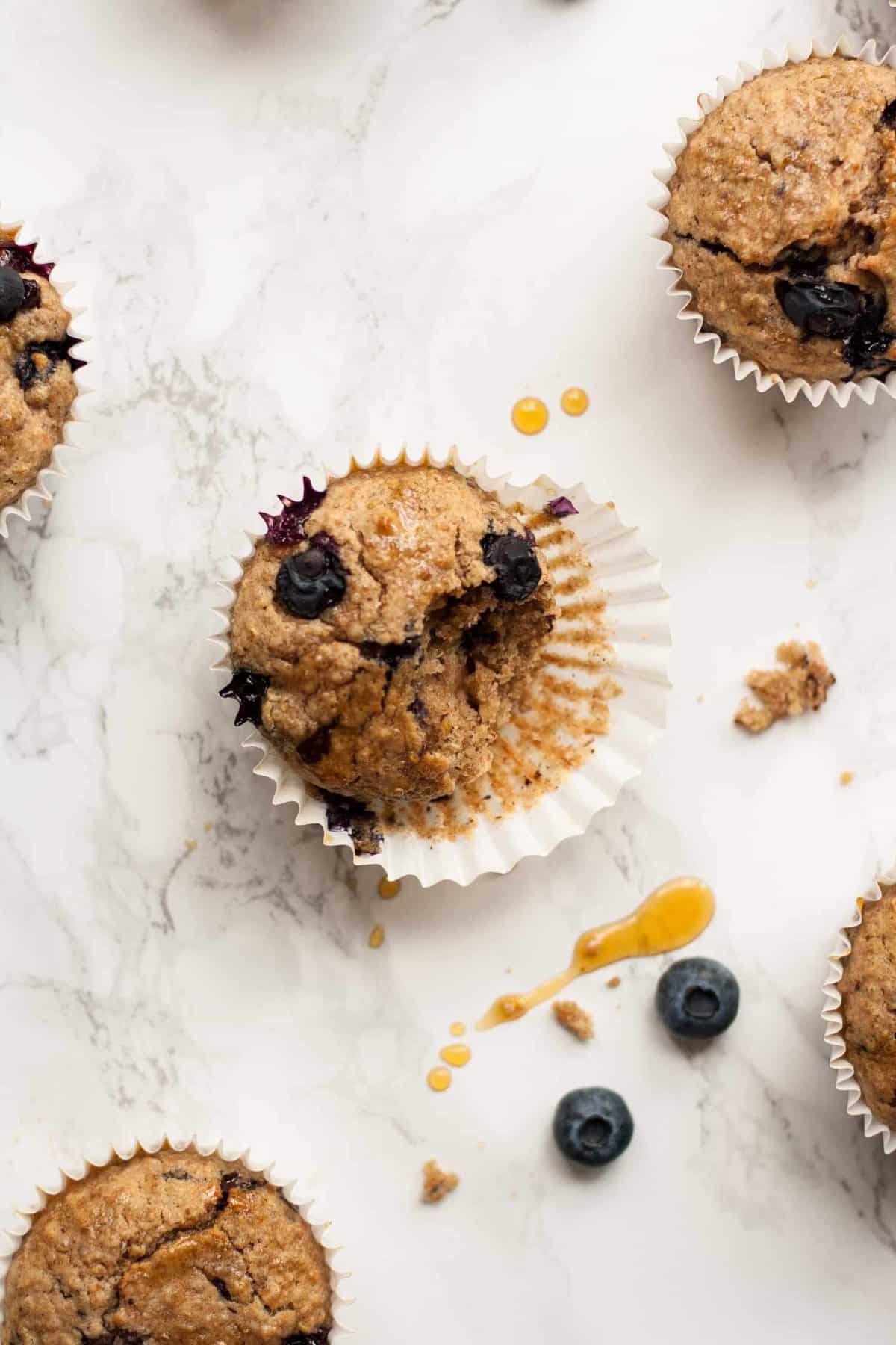 A breakfast blueberry muffin with case peeled and bitten into on a marble surface.