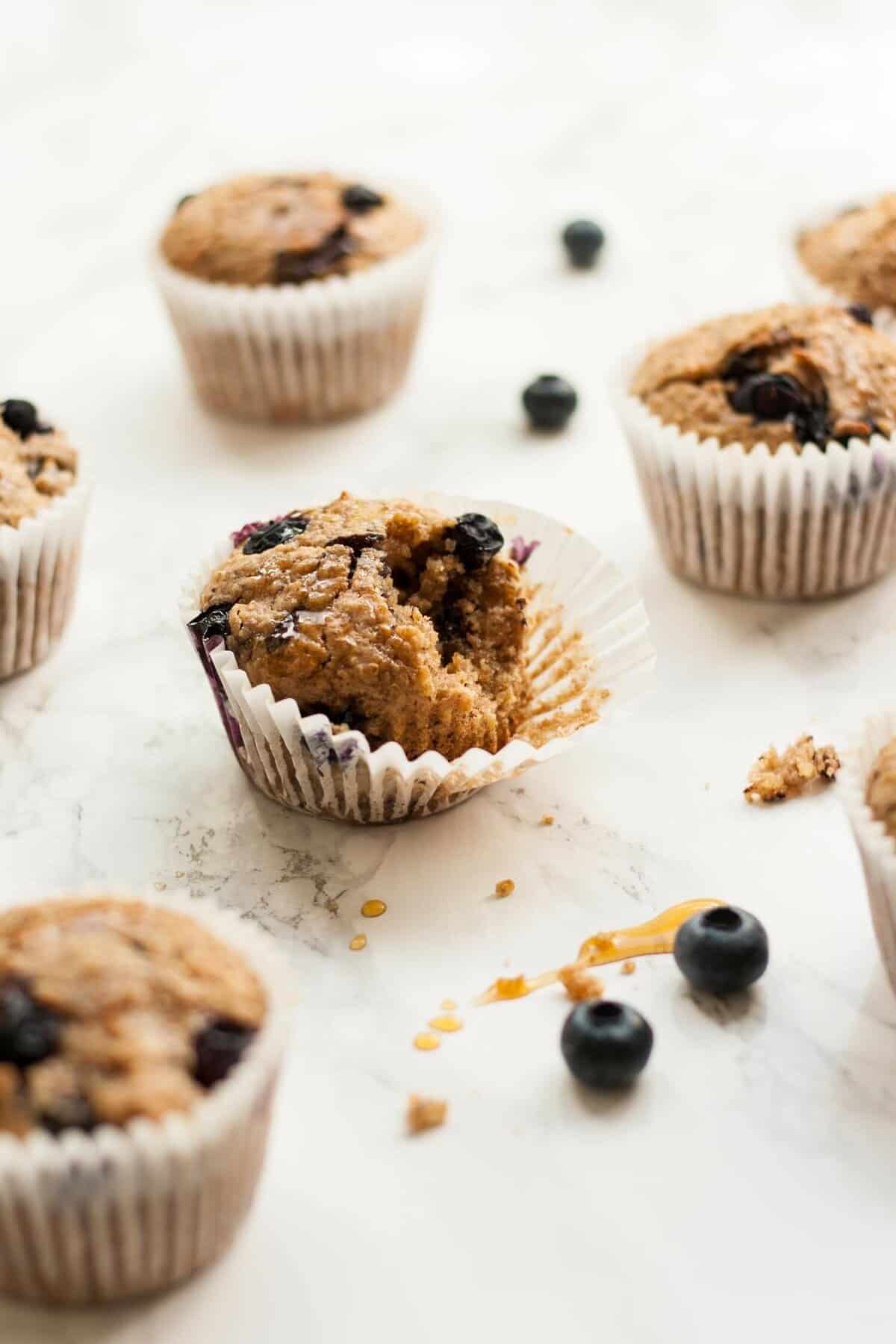 A marble surface with an array of blueberry muffins with blueberries and maple sauce around.