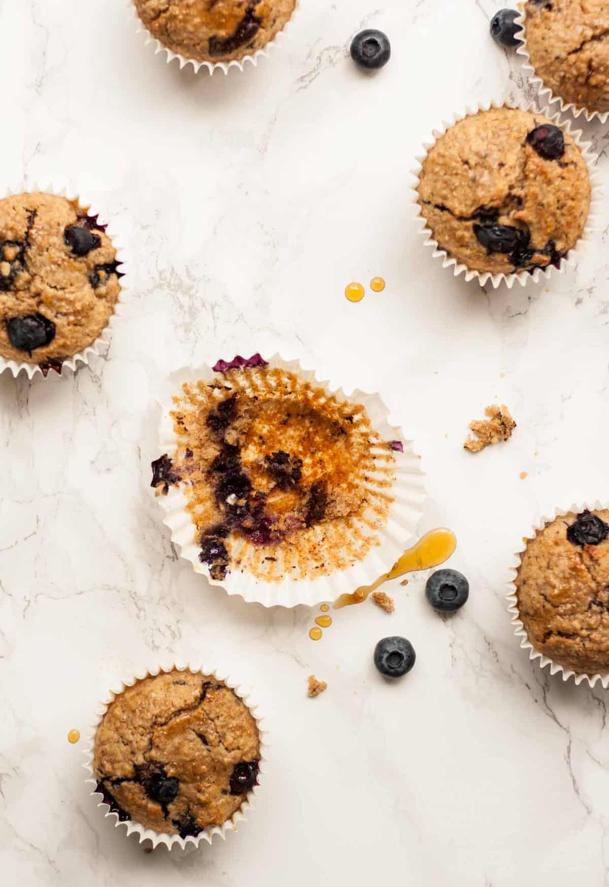 a blueberry muffin mostly eaten in it\'s case on a marble surface.