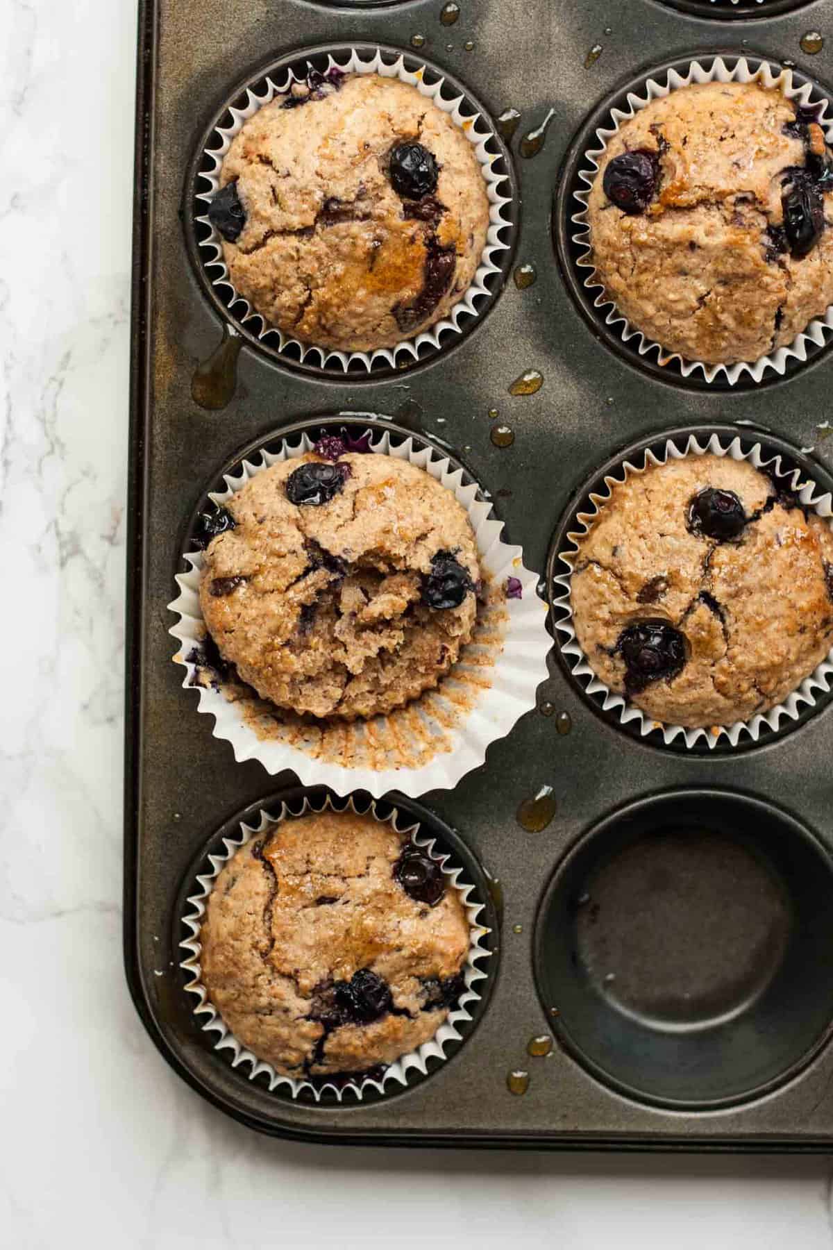 Close up of a bitten into blueberry muffin in a baking tray.