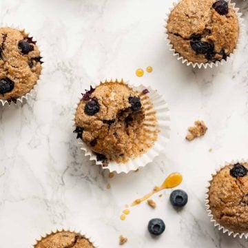 A broken open blueberry breakfast muffin sat on its case on a marble surface.