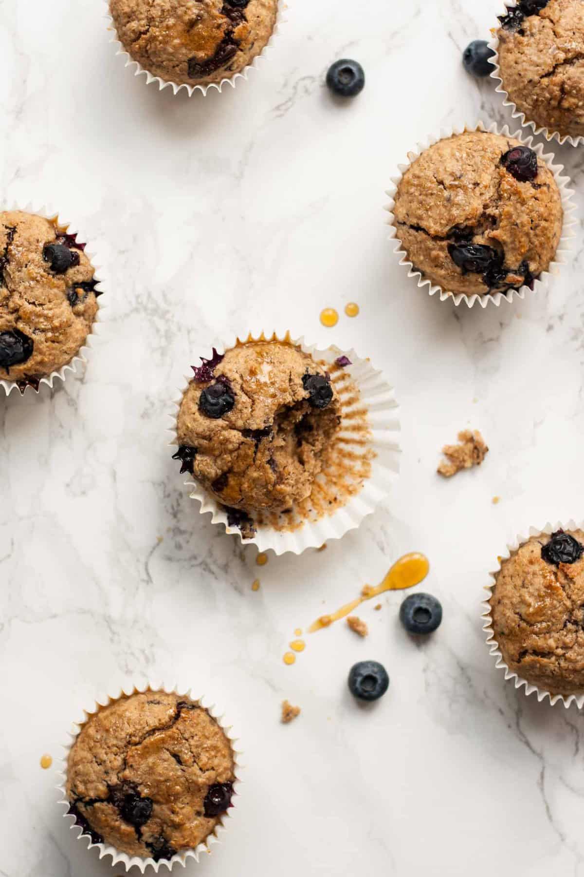 A broken open blueberry breakfast muffin sat on its case on a marble surface.