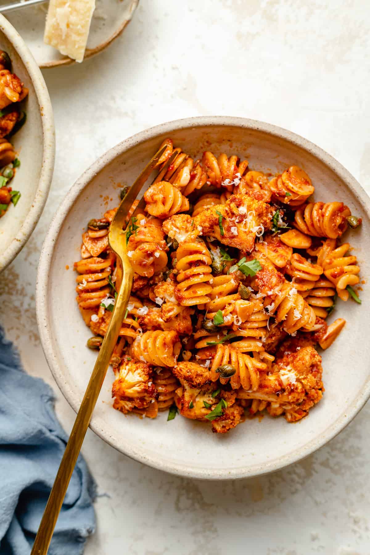 Nduja pasta with roasted cauliflower served in a bowl with a golden fork and a parmesan wedge to the side.