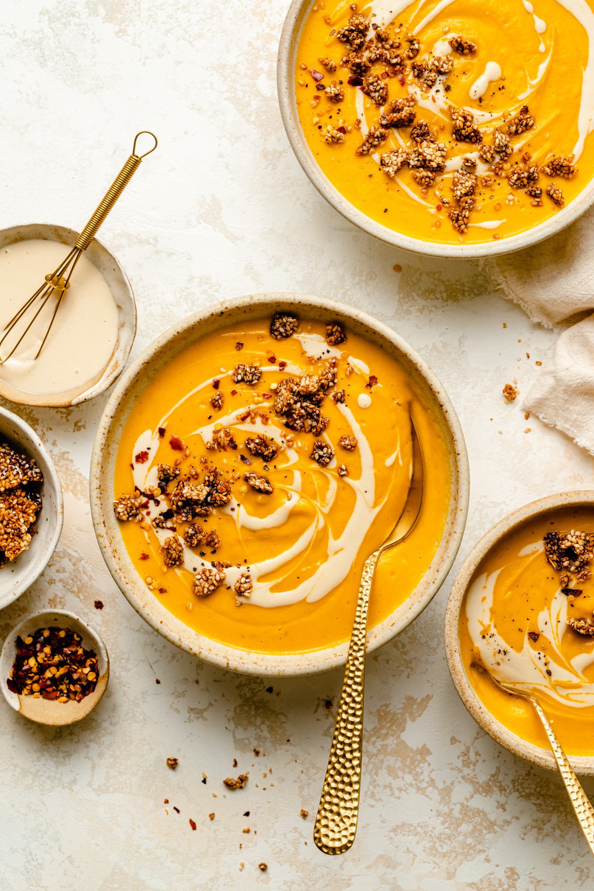 Sweet potato soup served in bowls and topped with a tahini swirl and sesame brittle.