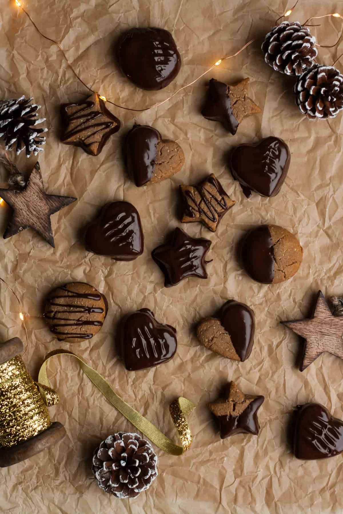 An array of chocolate lebkuchen cookies on a sheet of parchment paper with various decorations.