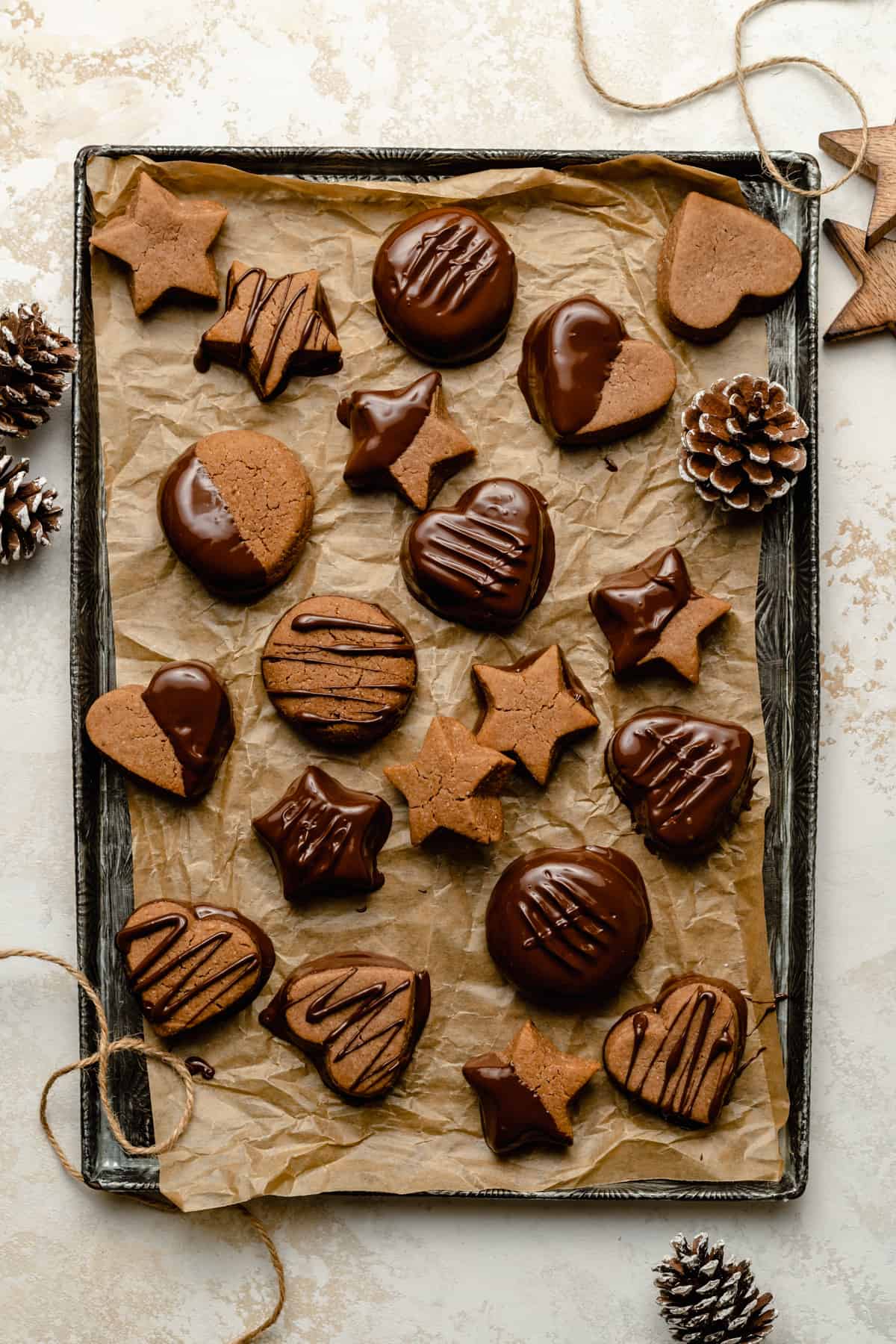 chocolate lebkuchen cookies arranged on a try with parchment paper, string and pine cones around. 