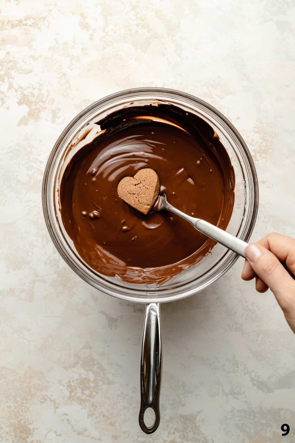 A lebkuchen cookie being dipped into a bowl of molten chocolate on a fork.