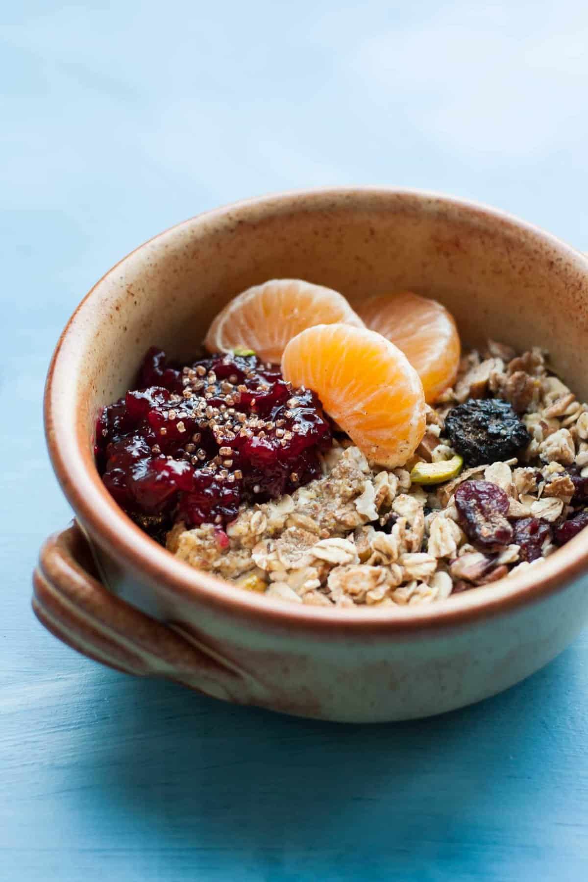 A close up of a bowl with Christmas muesli topped with jam and orange segments.