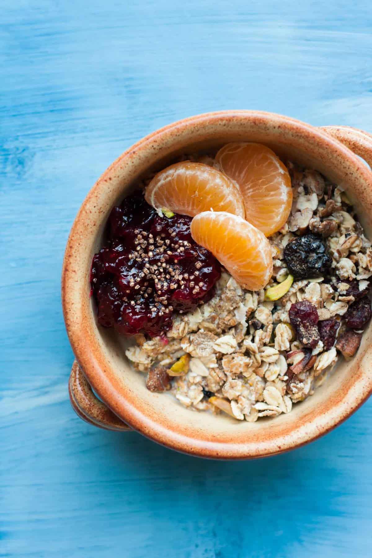 A bowl on a blue background with muesli, jam and orange segments on top.
