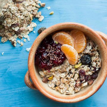 A bowl of museli topped with cranberry sauce, clementine segments with oats to the side.
