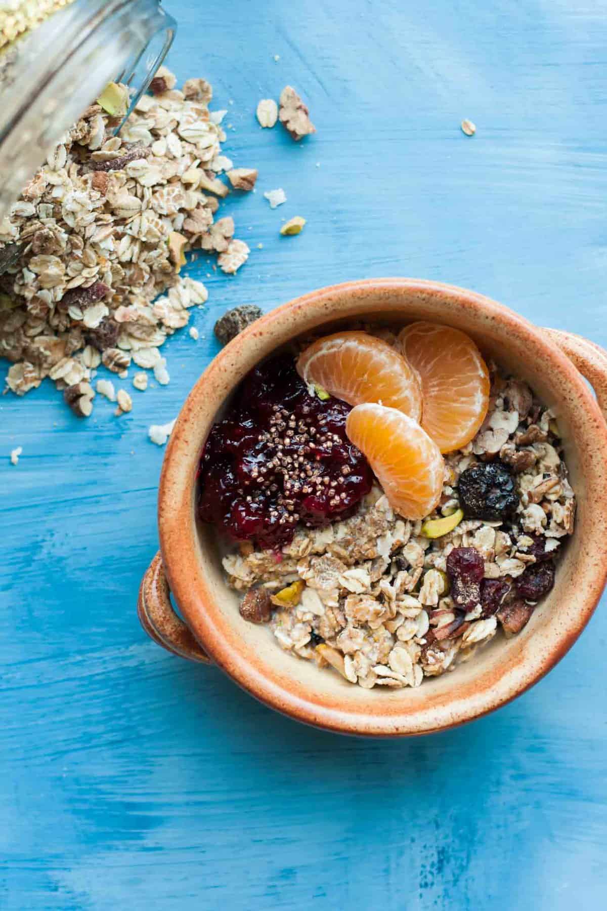 A bowl of museli topped with cranberry sauce, clementine segments with oats to the side.
