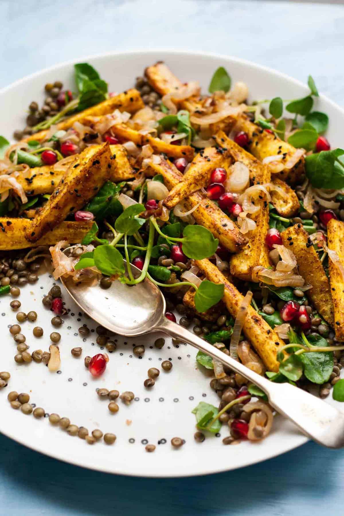 A close up of a spoon on a platter having served parsnip and lentil salad.