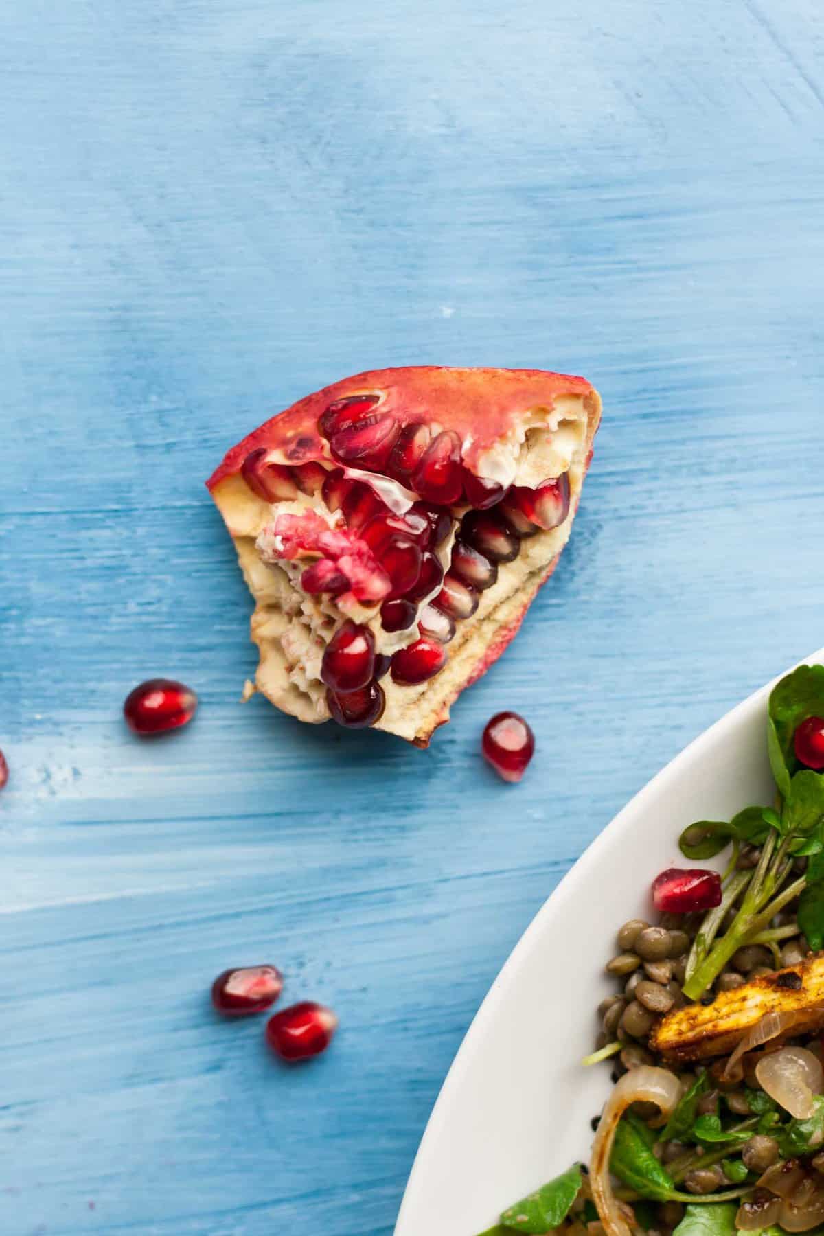 A close up of a broken up pomegranate with it\'s aryls falling out.