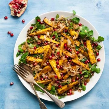 A serving plate with roasted spiced parsnips on top of a lentil salad with utensils.