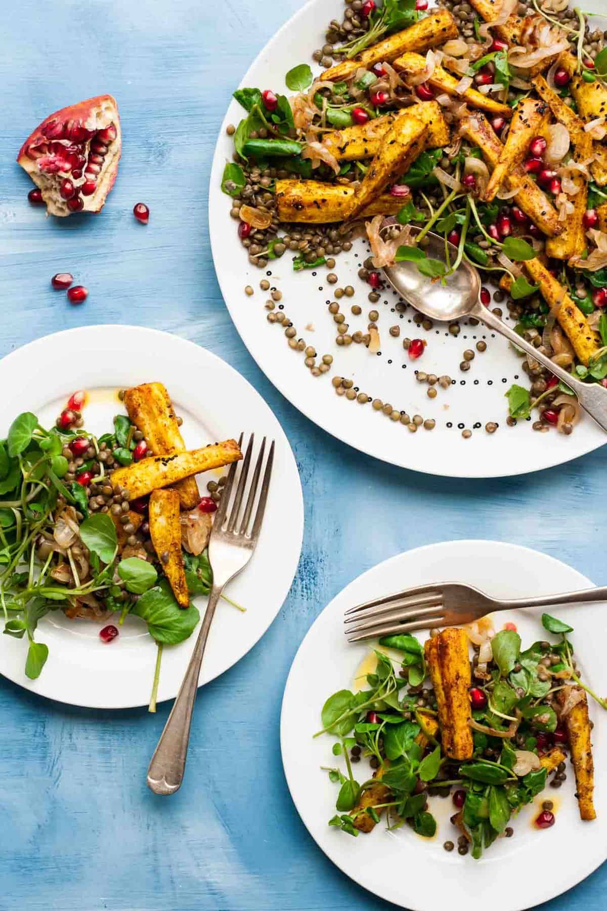 Two plates of served spiced parsnip and lentil salad with forks on the side.