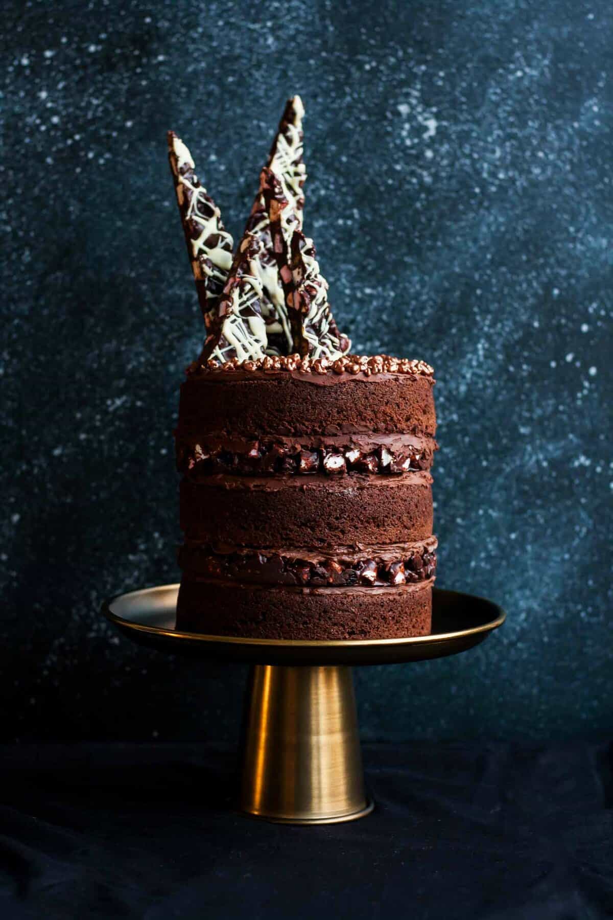 A triple layered chocolate rocky road layer cake with shards of rocky road on top.