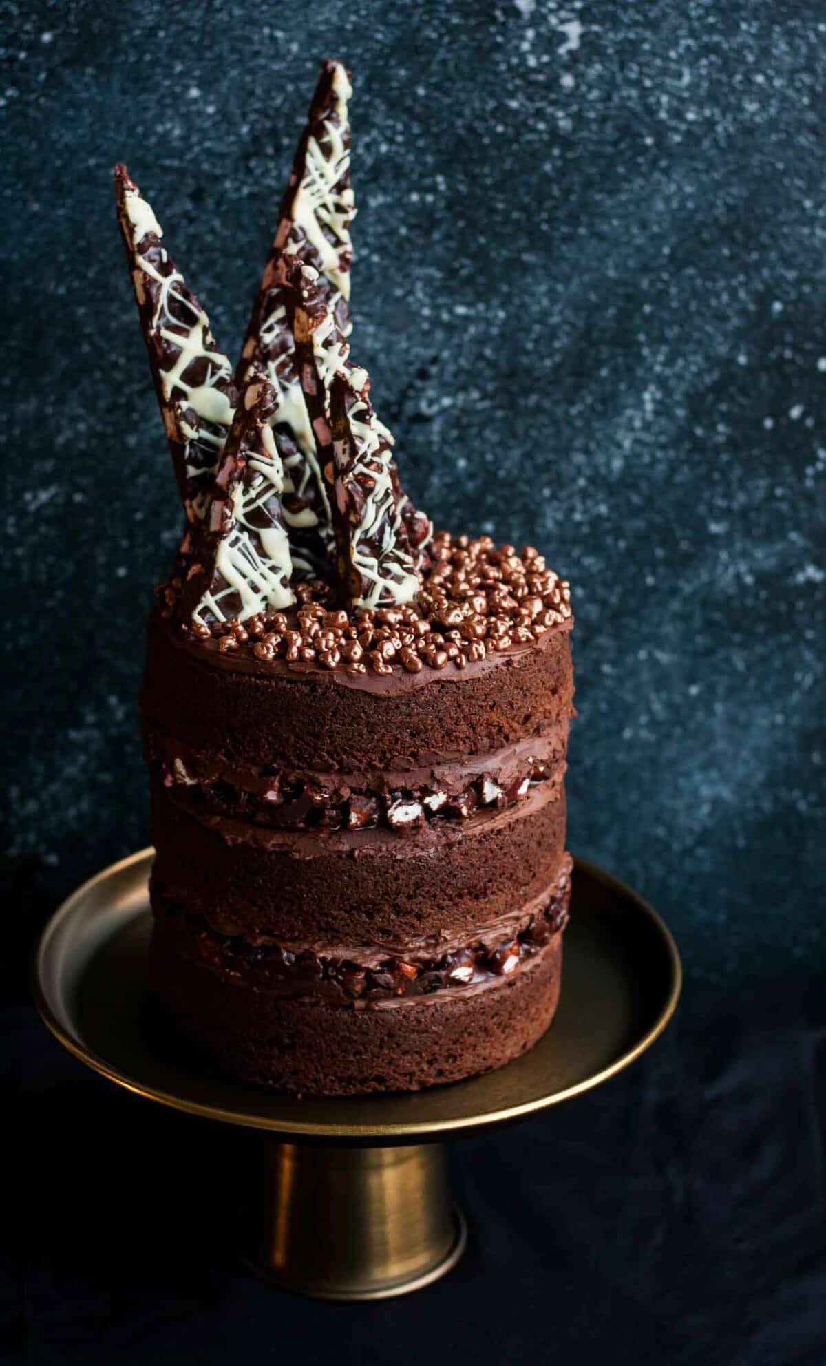 A close up of a triple layer rocky road cake on a golden cake stand.