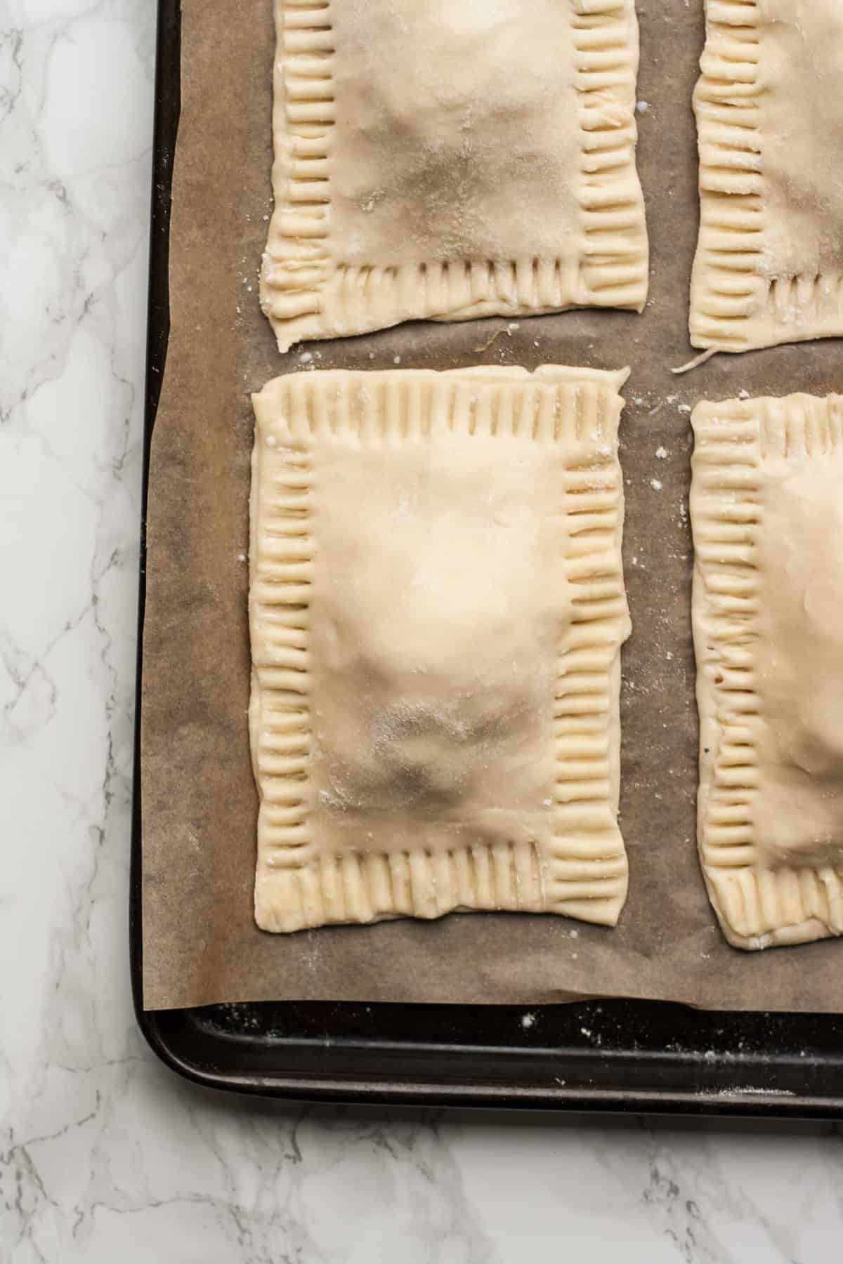 An unbaked turkey pastry with a fork crimped edge on baking sheet.